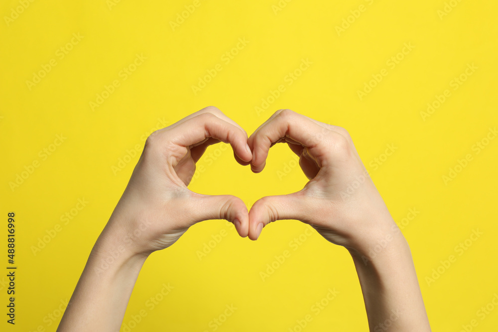 Obraz premium Woman making heart with her hands on yellow background, closeup