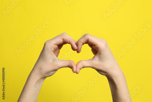 Woman making heart with her hands on yellow background  closeup