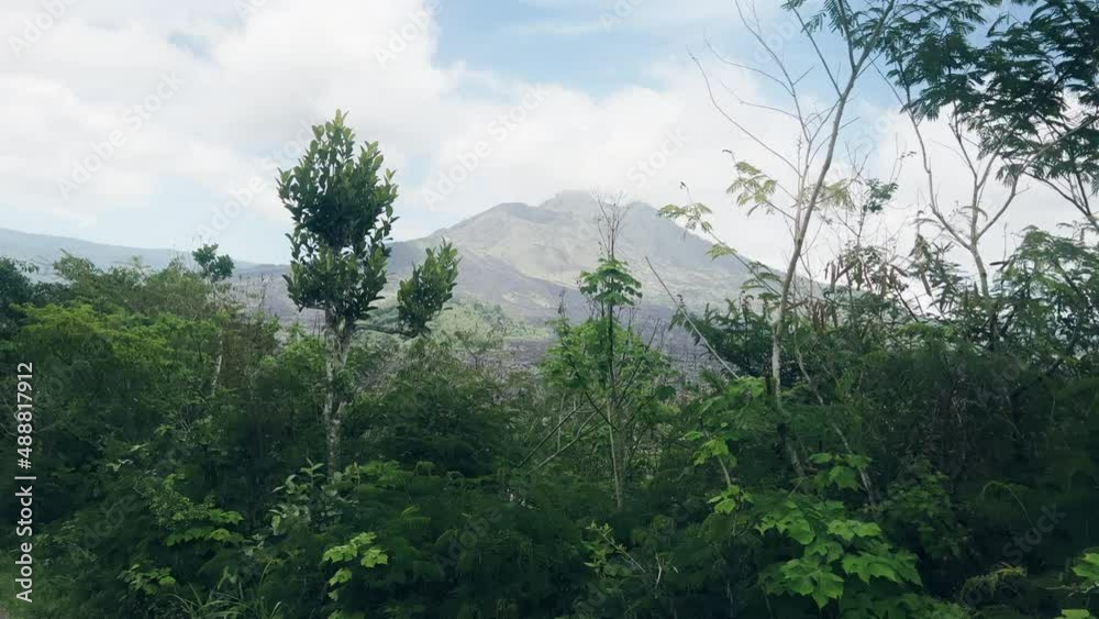 A view from eyes of a person driving along road and looking at a large volcano in distance through green thickets. Traveler looks at beautiful landscape with mountain and a cloudy sky while traveling. A view from eyes of a person driving along road and looking at a large volcano in distance through green thickets. Traveler looks at beautiful landscape with mountain and a cloudy sky while traveling.