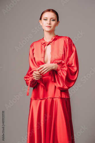 Candid of a young lady in red oversize dress with long wide sleeves and sexy neckline on grey studio background. Elegant contemporary female bohemian outfit.