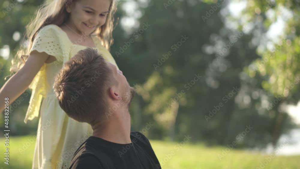 Absorbed Caucasian man sitting on park lawn surfing Internet as cheerful girl covering eyes with hands laughing. Portrait of young father with daughter resting outdoors on sunny day Absorbed Caucasian man sitting on park lawn surfing Internet as cheerful girl covering eyes with hands laughing. Portrait of young father with daughter resting outdoors on sunny day