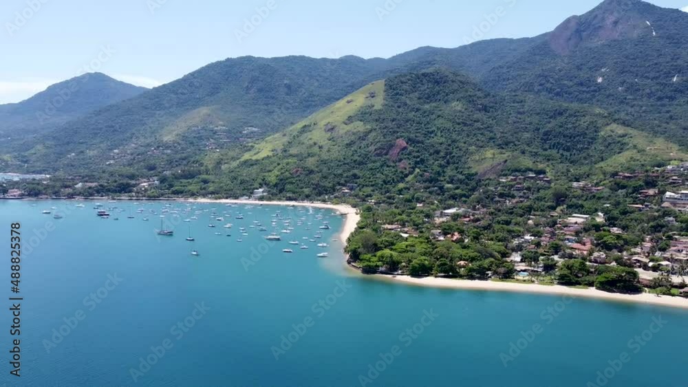 Town of Ilhabela and green mountains with beachfront at dusk with lights reflecting on the water. The Brazilian island has lush green forests and hills. Tourists gather on the beachfront all day. Town of Ilhabela and green mountains with beachfront at dusk with lights reflecting on the water. The Brazilian island has lush green forests and hills. Tourists gather on the beachfront all day.