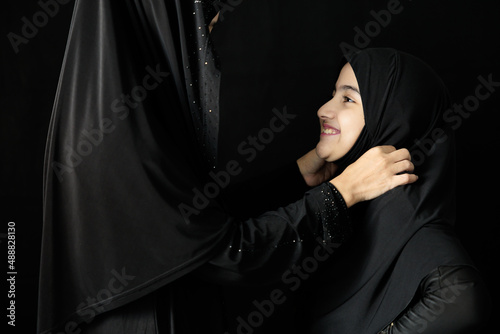 Foto muslim woman and her daughter smiling and hugging together on black background