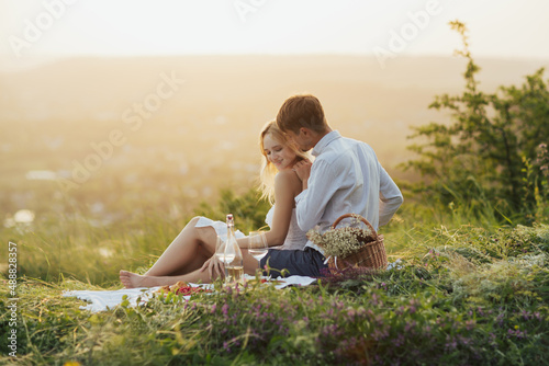 Cute couple on date sitting on the hill and enjoying summer picnic. Man embracing his woman from behind.
