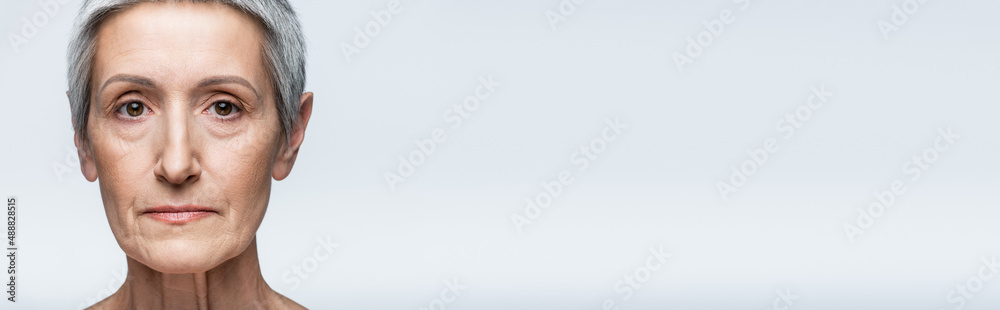 Obraz premium close up of mature woman with grey hair looking at camera isolated on grey, banner