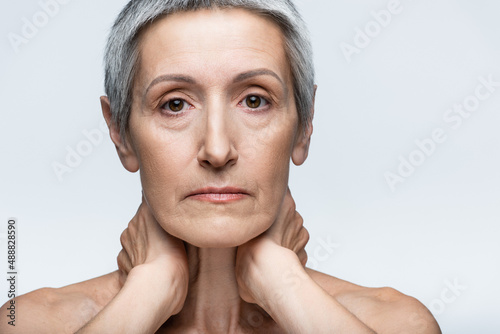 middle aged woman touching neck isolated on grey