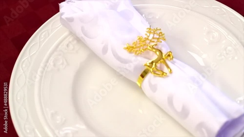 Gold metal Christmas reindeer napkin ring around white frilly napkin on layered traditional ceramic plates roatating photo
