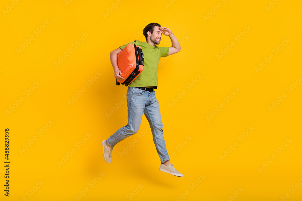 Full length profile side photo of young guy hold bag look empty space fly isolated over yellow color background Full length profile side photo of young guy hold bag look empty space fly isolated over yellow color background