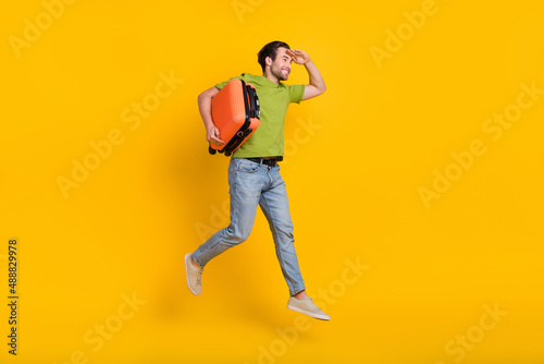 Full length profile side photo of young guy hold bag look empty space fly isolated over yellow color background