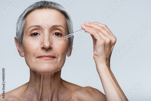 middle aged woman with grey hair holding pipette with serum isolated on grey
