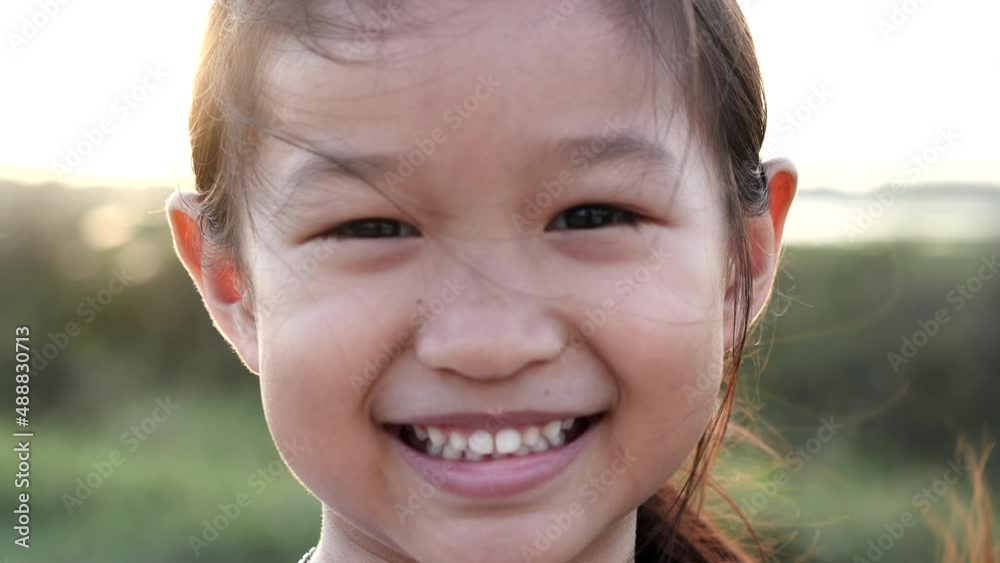 Portrait happy Asian little child girl smiling, laughing, looking at camera with beautiful sunset or sunrise in summer or spring nature outdoor background. Concept of portrait, happy children, family. Portrait happy Asian little child girl smiling, laughing, looking at camera with beautiful sunset or sunrise in summer or spring nature outdoor background. Concept of portrait, happy children, family.