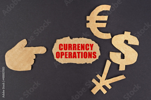 On a black surface, a figure of a hand, money symbols and torn cardboard with the inscription - currency operations photo