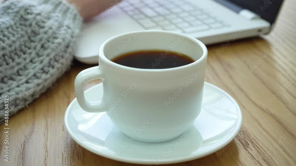 A large cup of hot coffee. Women's hands work on a laptop in a cafe A large cup of hot coffee. Women's hands work on a laptop in a cafe