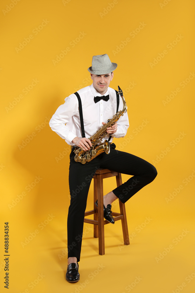 Naklejka premium Young man in elegant outfit with saxophone on yellow background