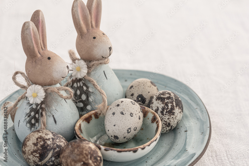 Quail eggs and blue Easter rabbits on blue ceramic plates on white table. Easter table decoration Quail eggs and blue Easter rabbits on blue ceramic plates on white table. Easter table decoration