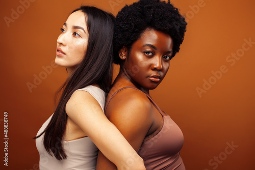 young pretty asian, african american woman posing cheerful together on brown background, lifestyle diverse nationality people concept