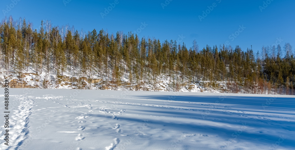 Obraz premium Winter landscape with frozen and snow-covered lake, trees and blue sky in winter