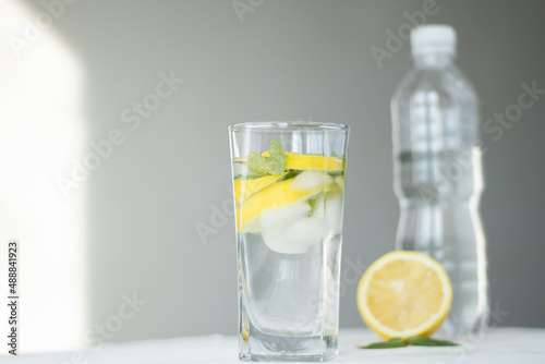 glass of water with lemon and ice and mint on blue background and white table