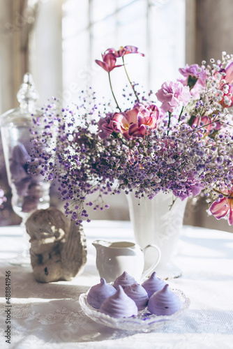 table set in lilac tones very peri color of the year 2022 with candle, statuette angel, purple marshmallow, butterfly and lilac gypsophila flowers, vintage decor in retro loft style room, celebration