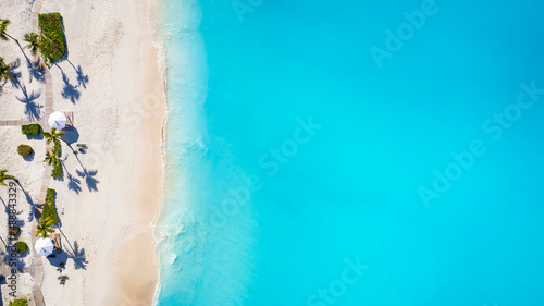 Aerial top down view of a tropical paradise beach with fine sand, cocnut palm trees and turquoise shining sea in the Caribbean with copy space