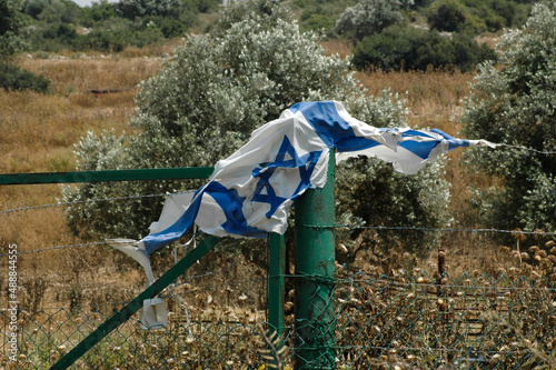 A torn and shredded blue and white flag of the State of Israel caught on a barbed wire fence. photo