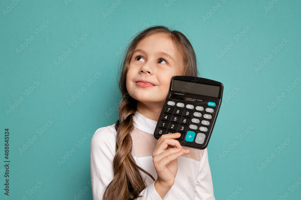 Portrait of a serious little girl holding a calculator on a blue background. Portrait of a serious little girl holding a calculator on a blue background.