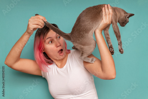 Surprised young woman looks under the tail of her pet cat