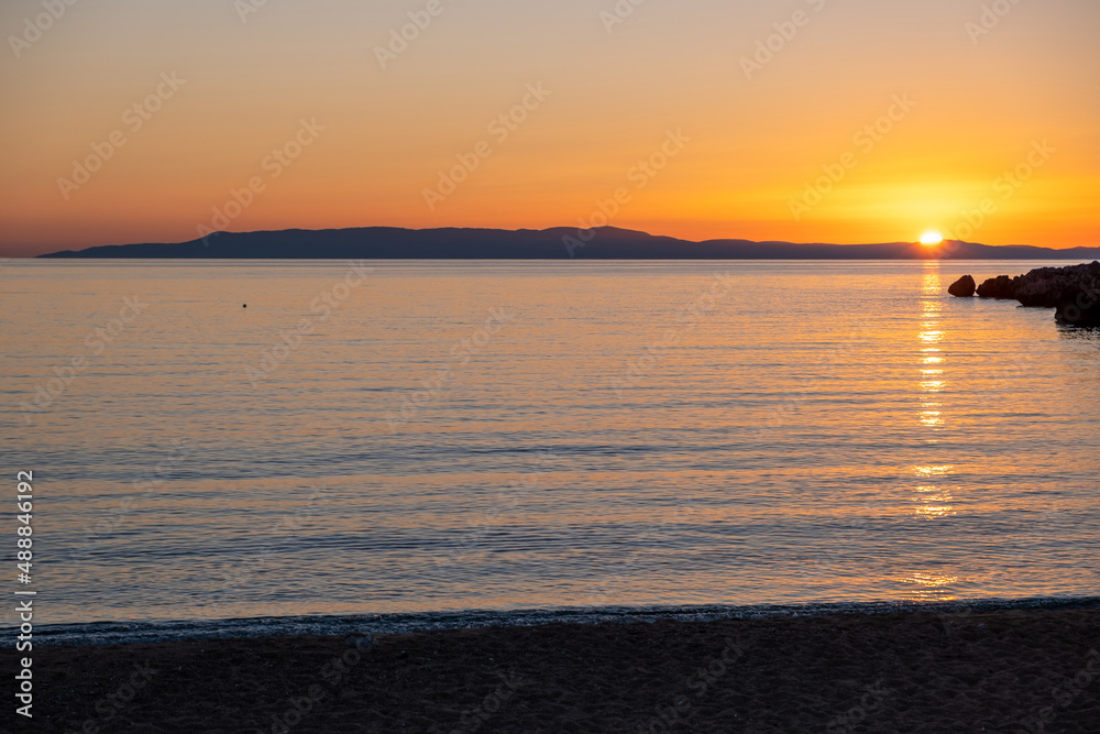 Sandy beach at sunset. Greece. Sundown over calm sea, reflection and orange color sky.