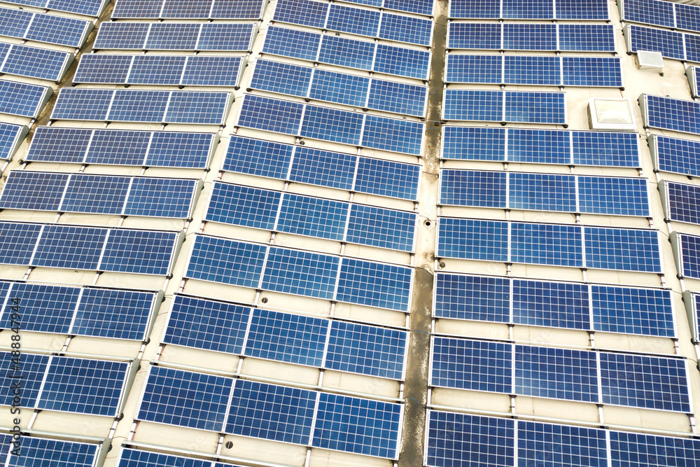 Aerial view of solar power plant with blue photovoltaic panels mounted of industrial building roof.