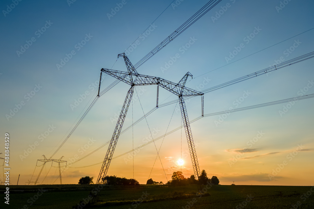 Dark silhouette of high voltage towers with electric power lines at sunrise