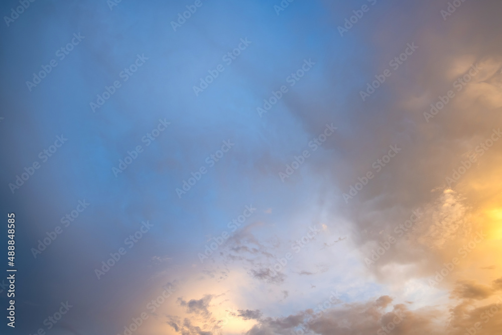 Dramatic moody sunset landscape with puffy clouds lit by yellow setting sun and blue sky.