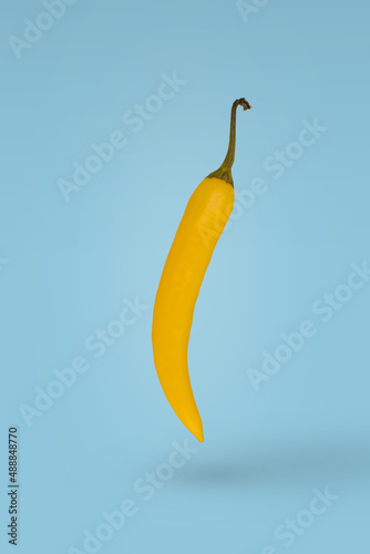 Yellow hot chili pepper floating in air isolated on blue background.