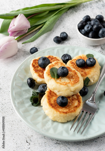 Cottage cheese fritters with blueberries on concrete background with copy space with tulips