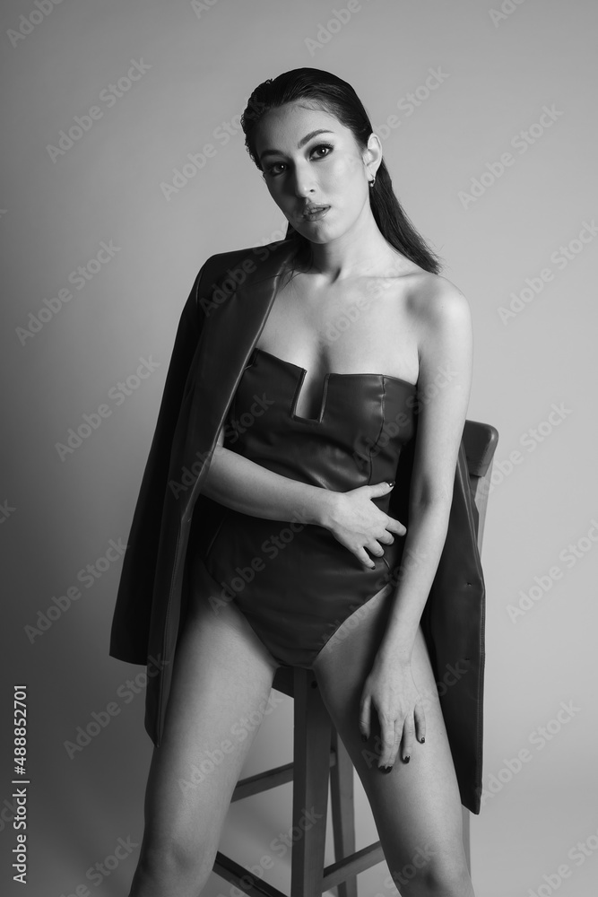 fashionable beautiful sexy woman model in a leather bodysuit and jacket of Asian appearance is standing in the studio in black and white