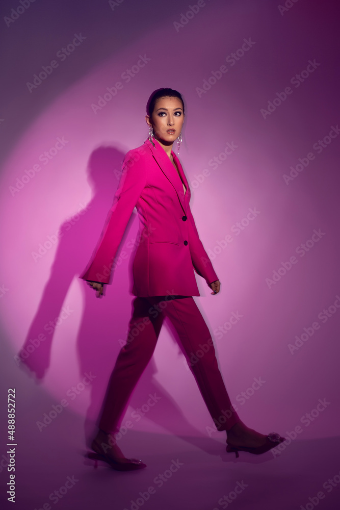 fashionable sexy woman model of Asian appearance in a business pink suit on the background in the studio fashionable sexy woman model of Asian appearance in a business pink suit on the background in the studio