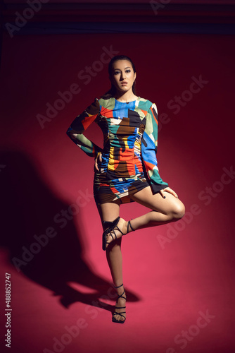 sexy asian young fashionable woman model in a multicolored short dress on a red background in the studio