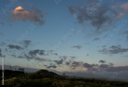 A green hump, spoil from an old mine, seen next to a black barn against sunlit, evening clouds in autumn in the North Pennines