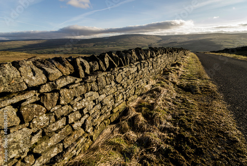 A dry stone wall in winter sunlight, leading into the distance alongside a country lane in the North Pennines, County Durham, England