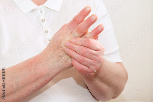 An elderly woman suffering from pain in her fingers close-up. An elderly lady touches her hand, joint pain, joint problems. An elderly woman is holding her sore hand.