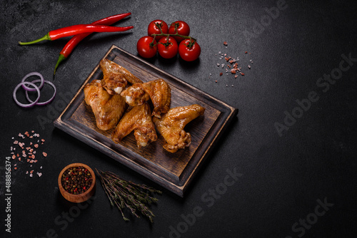 Baked chicken wings with vegetables and spices on a black background