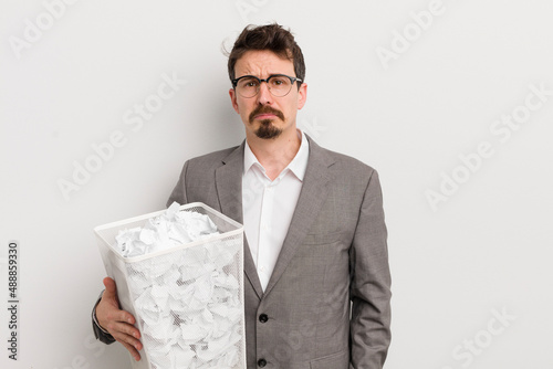 young handsome man feeling sad and whiney with an unhappy look and crying. paper balls basket concept photo