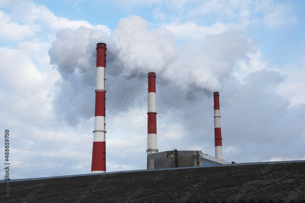 Thermal power plant with three pipes in the background and blue sky polluting the environment.