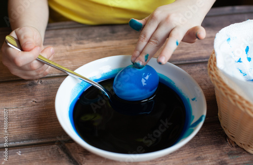 girl in a plate with paint paints an egg blue. Easter