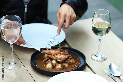 Hands cutting chicken with potatoes and sauce on black plate and wood table