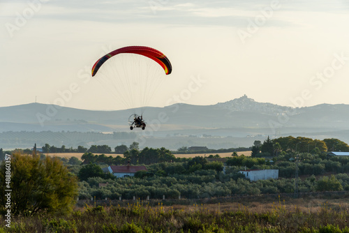 Side view of a paramotor vehicle flying near the ground with green and mountains behind