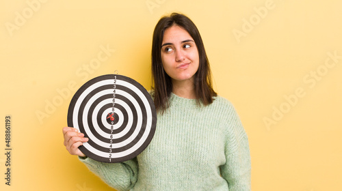 young hispanic woman thinking, feeling doubtful and confused. darts target concept photo