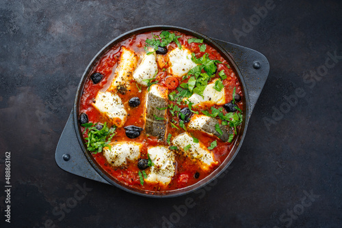 Traditional Spanish seafood zarzuela de pescado with fish served in red sauce as top view in design pot