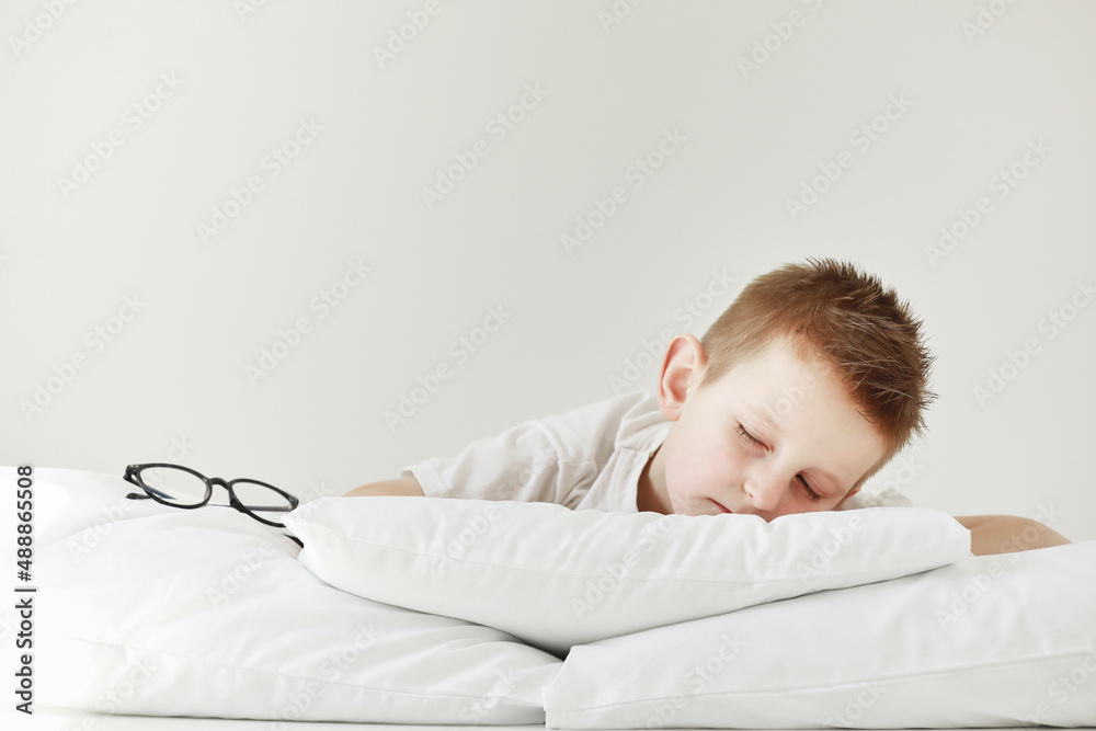 Adorable little boy sleeping in bed. morning dreaming on white bed. glasses from the side Adorable little boy sleeping in bed. morning dreaming on white bed. glasses from the side