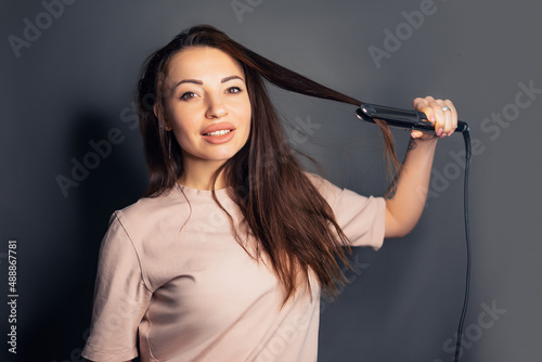 Portrait of charming girl using straightener for curly hair making styling isolated over white background preparing for party. Wellbeing wellness pampering concept