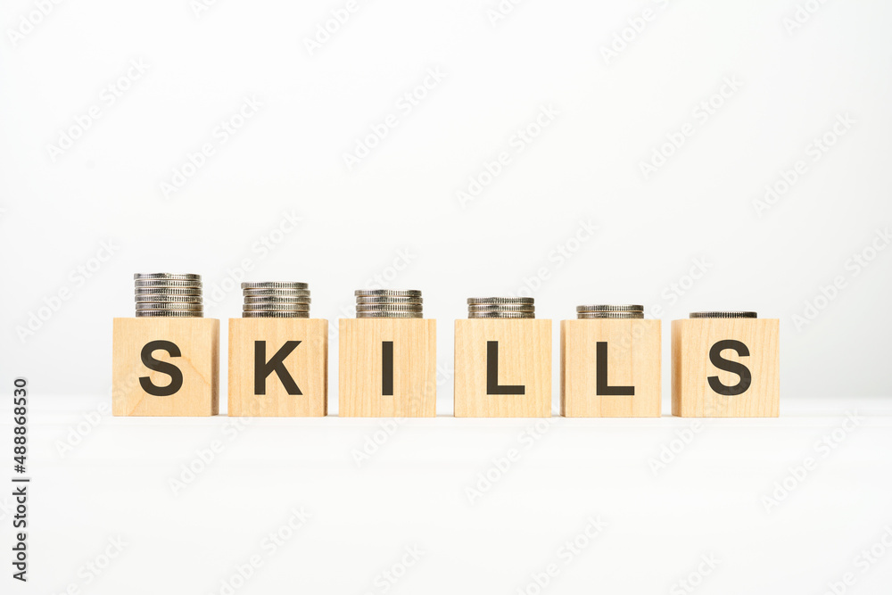 SKILLS text written on wooden block with stacked coins on white background SKILLS text written on wooden block with stacked coins on white background